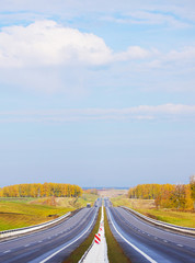 Straight highway among autumn fields in the sunny bright day