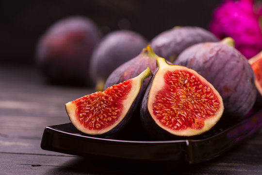 Ripe delicious figs and autumn flowers on black wooden background. Selective focus
