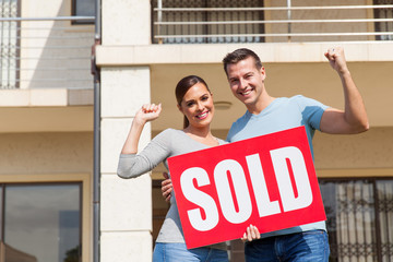 young couple holding sold sign in front of their old house