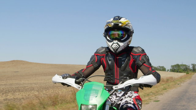 Motocross biker riding enduro motorcycle on country road front view medium shot