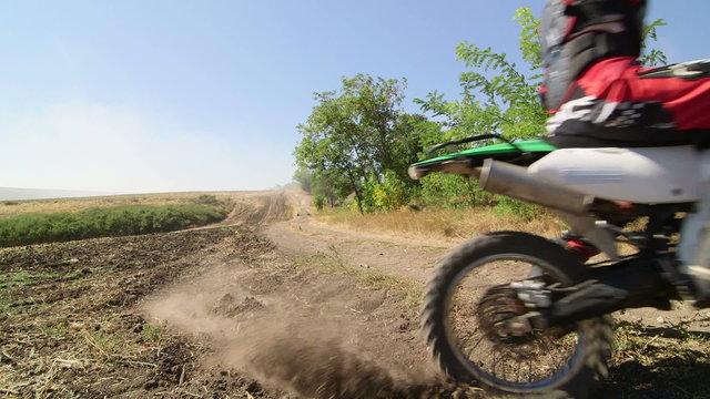 Motocross racer starting engine of his dirt bike riding away kicking up dust