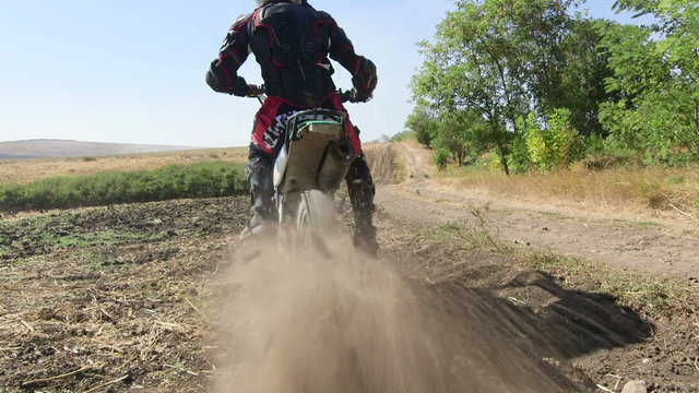 Motocross racer start riding his dirt bike kicking up dust rear view jib crane shot