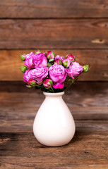 Obraz premium pink roses in a vase on wooden background. flowers
