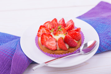 cake with strawberries and custard on a white plate with a spoon. on colored napkin. top view. Portion baking, linen napkins