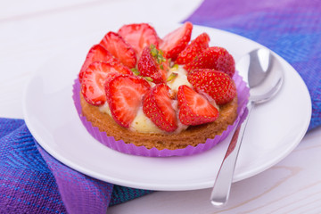 cake with strawberries and custard on a white plate with a spoon. on colored napkin. top view. Portion baking, linen napkins