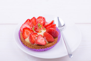 cake with strawberries and custard on a white plate with a spoon. on a light wooden background. top view. Portion pastries