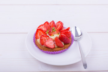 cake with strawberries and custard on a white plate with a spoon. on a light wooden background. top view. Portion pastries