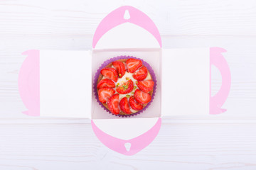 cake with strawberries and custard in a box for shipping. on a light wooden background. top view. Portion pastries