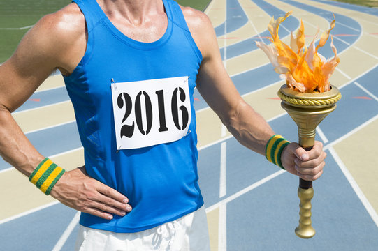 Athlete wearing 2016 race bib holding sport torch in front of running track