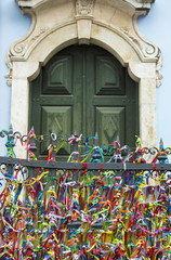 Fototapeta na wymiar Old colonial church door in Pelourinho, Salvador, Brazil is framed by a fence decorated with colorful Brazilian wish bracelets