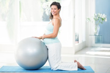 Pregnant woman with exercise ball kneeing on mat