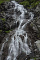 Fototapeta na wymiar Fast mountain waterfall in vertical orientation