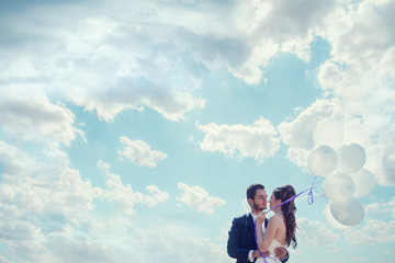 Just married bride and groom with baloons in hand over cloudy sk