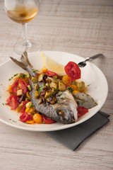 Fried dorado with vegetables  on the ceramic plate with glass of vine vertical