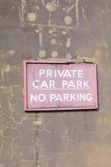 Faded and cracked wooden 'Private Car Park - No Parking' sign on wall