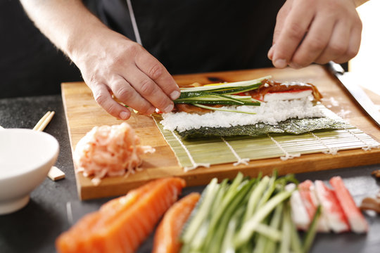 Sushi , etapy przygotowywania sushi z łososiem, paluszkiem krabowym, og&oacute;rkiem tykwą zawiniętego w glon nori