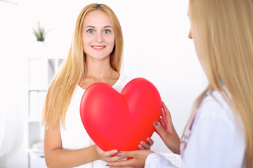 Woman doctor  in  hospital, a large red heart  in patient hand  at the background