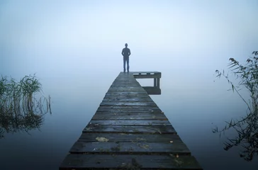 Fototapeten Mann, der an einem nebligen, grauen Morgen auf einem Steg an einem See steht. © sanderstock