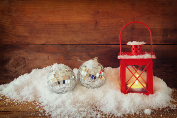 christmas background with red lantern, bauble and snow over wooden background
