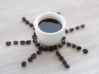 Cup of espresso coffee on gray wooden table with coffee beans creating sunbeam around the cup