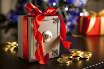 Little safe with red ribbon, golden coins on dark surface. Christmas tree with beautiful...