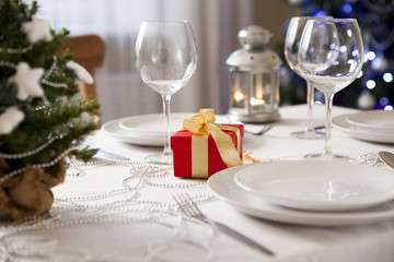 Beautiful christmas table served and decorated with candles. Christmas tree with lights on the background