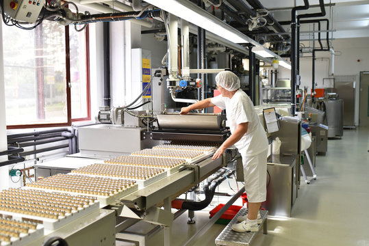 Frau bedient Maschine in der Lebensmittelindustrie - Fabrik zur Herstellung von Pralinen - Fliessband mit Süßwaren