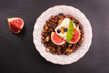 Healthy breakfast: bowl of chocolate balls with yoghurt and fresh figs on black stone table. Selective focus