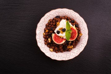 Healthy breakfast: bowl of chocolate balls with yoghurt and fresh figs on black stone table. Selective focus