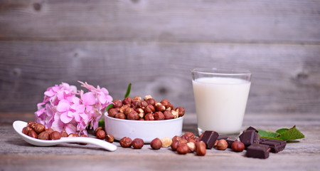 Fresh hazelnut, dark chocolate and glass of milk on wooden table