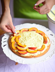 Woman hand put peach on the cake crust