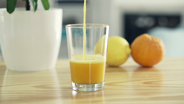 Pouring orange juice into glass on table at home, slow motion 240fps

