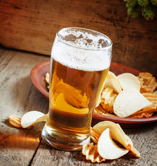 large glass of light beer and potato chips on a wooden backgroun