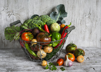 fresh garden vegetables - broccoli, zucchini, eggplant, peppers, beets, tomatoes, onions, garlic - vintage metal basket on a light wooden background