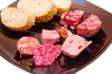 Pieces of salami and bread slices on plate on white background close