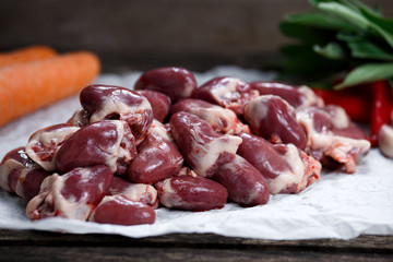 Raw Duck hearts on crumpled paper, decorated with vegetables. on old wooden table