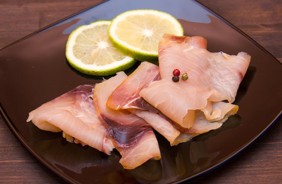 Smoked swordfish on black plate on wooden table seen close