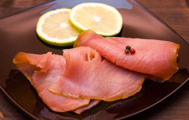 Smoked tuna on black plate on wooden table seen close