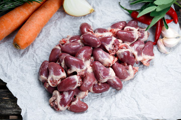 Raw Duck hearts on crumpled paper, decorated with vegetables. on old wooden table