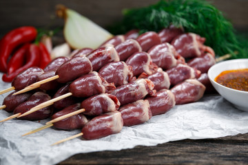 Ready to cook Duck Heart stringed on skewers BBQ with hot sauce and chili pepper. decorated with greens and vegetables. background