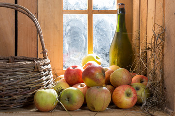 bottle and glass of cider with apples near the window