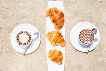 Two cups of coffee with latte art and croissants