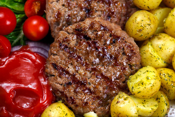 Close up Fresh juicy grill burgers, served with ketchup, young potatoes, tomatoes and vegetables. On wooden table