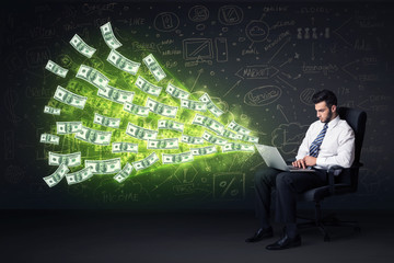 Businessman sitting in chair holding laptop with dollar bills co