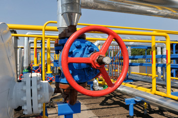 Red faucet with steel pipe in natural gas treatment plant in bright sunny summer day