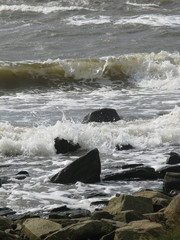 Rocky coastal landscape with seaspray at Skrea Strand on a sunny and windy day with dark clouds in Falkenberg, Sweden.