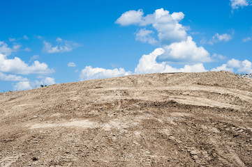 Sandy dirt hill with tracks against clouds and sky