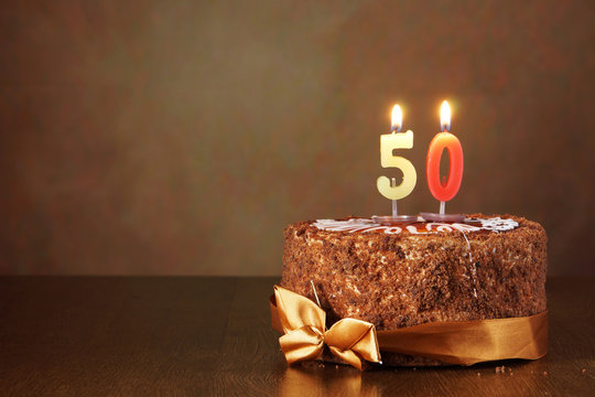 Birthday chocolate cake with burning candles as a number fifty on brown background