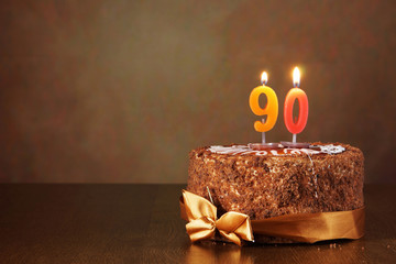 Birthday chocolate cake with burning candles as a number ninety on brown background