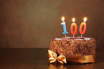 Birthday chocolate cake with burning candles as a number one hundred on brown background